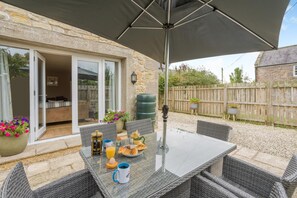 An outdoor patio with a table set for breakfast, wicker chairs, and a large umbrella. - 3 Bed in Scremerston (oc-w42466) (Scremerston)