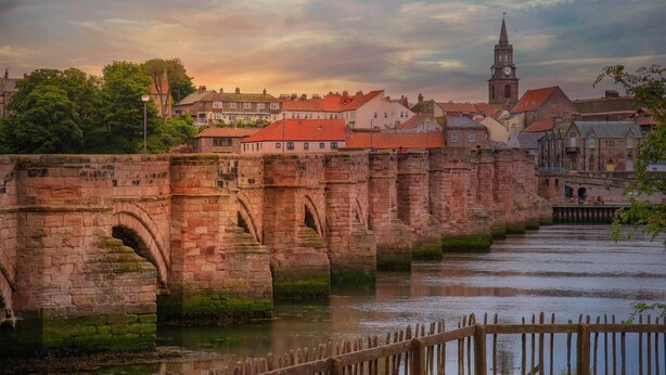 Uma ponte de pedra sobre um rio, com edifícios históricos ao fundo.