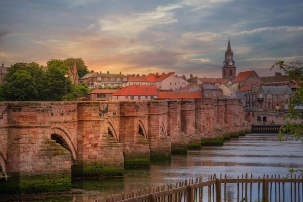 A stone bridge over a river with historic buildings in the background. - 3 Bed in Scremerston (oc-w42466) (Scremerston)