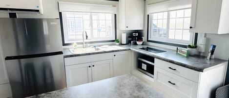 Una cocina moderna con armarios blancos, encimeras de granito, un refrigerador de acero inoxidable y un ventanal que proporciona luz natural.