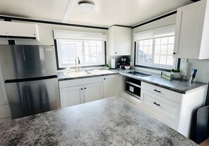 Una cocina moderna con armarios blancos, encimeras de granito, un refrigerador de acero inoxidable y un ventanal que proporciona luz natural.