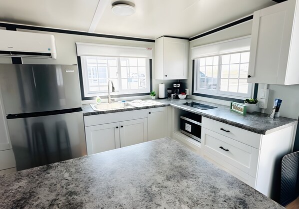 A modern kitchen with white cabinets, granite countertops, a stainless steel refrigerator, and a window providing natural light.