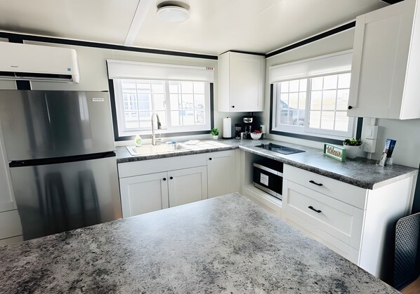 Una cocina moderna con armarios blancos, encimeras de granito, un refrigerador de acero inoxidable y un ventanal que proporciona luz natural.