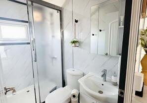 Un baño moderno con cabina de ducha de vidrio, inodoro, lavamanos y espejo.
