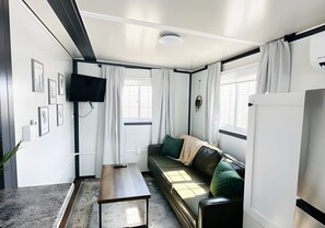 A compact living space with a sofa, a flat-screen TV, a small table, and a refrigerator.