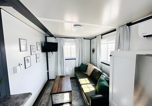Een knus woongedeelte met een bank, een tafel, een televisie en afbeeldingen in lijsten aan de muren.