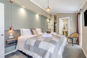 A modern hotel room with a large bed, bedside tables, a chair, a mirror, and a bathroom visible through an open door. - 2 Bed in Burnham Market (oc-s42081) (Burnham Market)