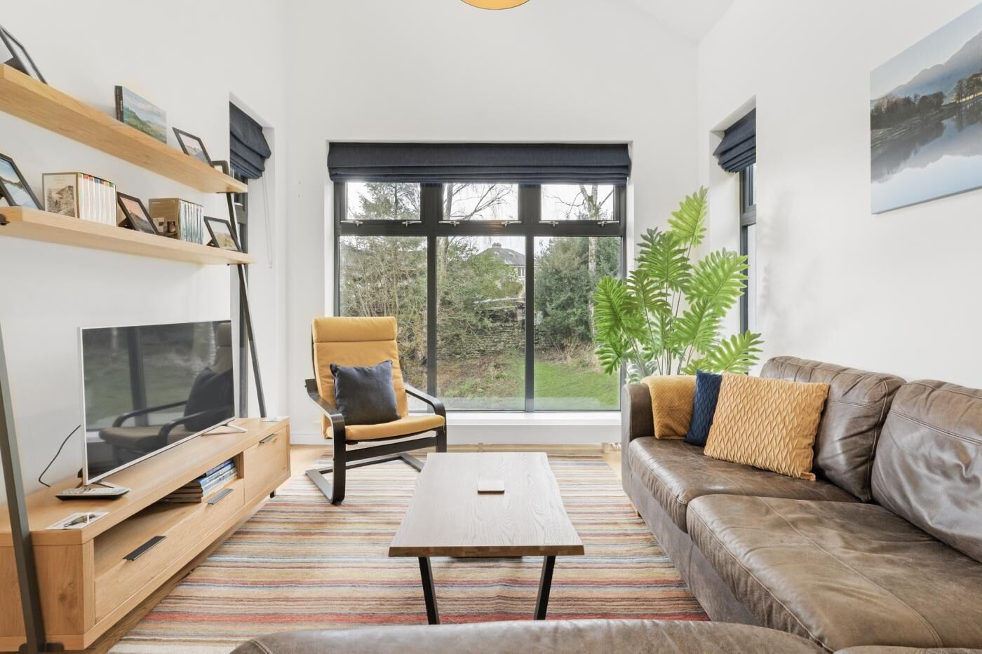 A modern living room with a television, sofa, armchair, and large windows.