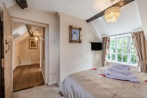 Une chambre à coucher avec un lit, une fenêtre avec des rideaux, un lustre et une porte donnant sur une autre pièce.