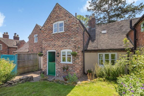 Une maison en briques avec une porte verte, un petit jardin et une maison voisine.
