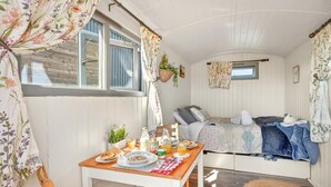 A cozy room with a wooden table set for breakfast, a bed with a blue blanket, and a window with curtains.