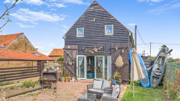Una casa con tetto spiovente, un patio con mobili da esterno e kayak riposti all'aperto.