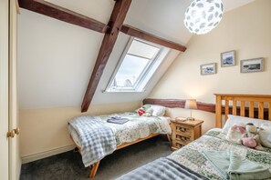 Une chambre avec deux lits, un plafond en pente, un puits de lumière et une tête de lit en bois.
