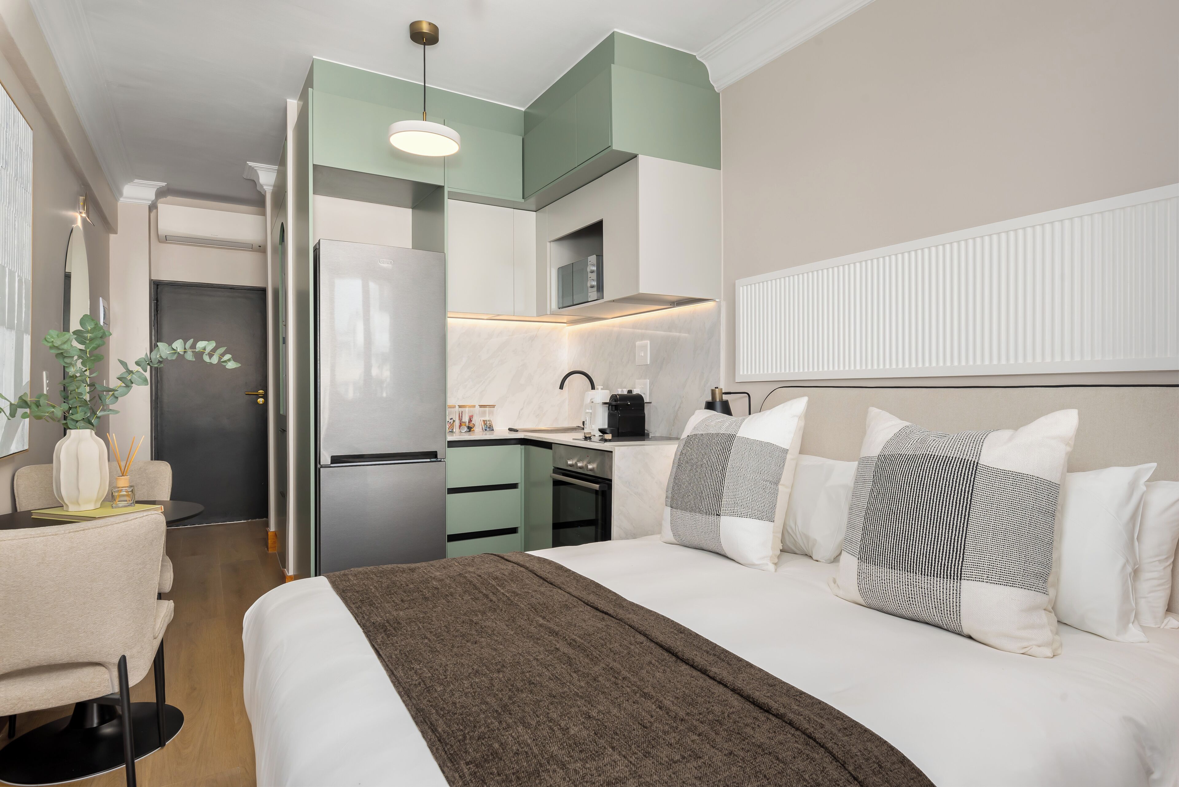 Een moderne hotelkamer met een bed, nachtkastje en een kitchenette.