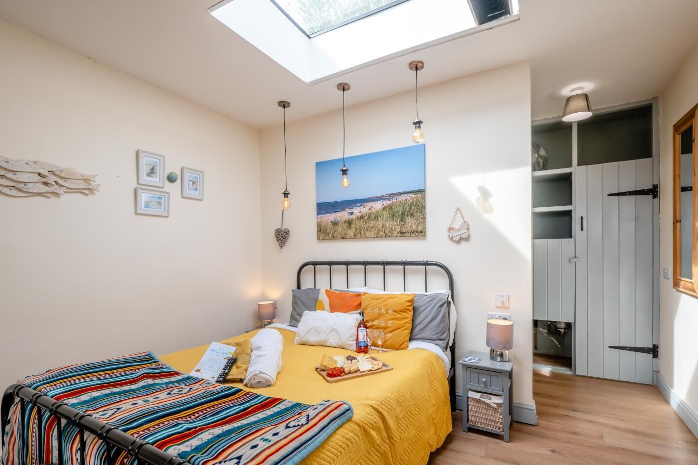 Camera da letto con finestra sul tetto, letto con biancheria colorata, lampade da comodino, un quadro e un armadio.