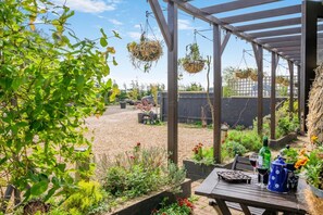 Un patio couvert agrémenté de jardinières suspendues, d’une table avec un verre à vin et offrant une vue sur le jardin.
