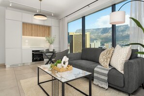 Una sala de estar moderna con un sofá gris, una mesa de centro de mármol y vistas a un paisaje urbano a través de amplios ventanales.