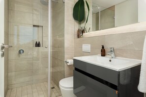 Un baño moderno con cabina de ducha de vidrio, inodoro blanco, tocador con lavamanos y espejo.