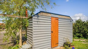 Ein kleines, eingeschossiges Gartenhaus mit Holztür und geneigtem Dach.