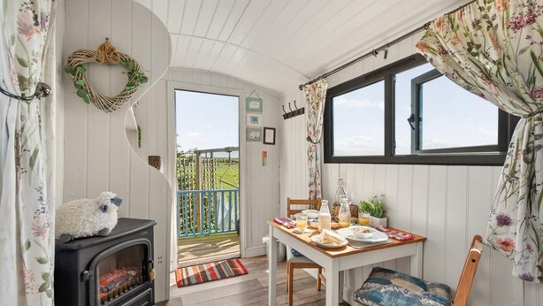 Ein gemütliches Zimmer mit Kamin, einem für das Frühstück gedeckten Esstisch und Blick ins Freie.