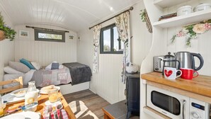 Ein gemütliches Interieur mit einem Bett, einem Frühstückstisch, einer Küchenzeile und einem Fenster mit Vorhängen.