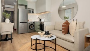 Un espace de vie compact comprenant un coin cuisine, un canapé, une table basse et un miroir rond.