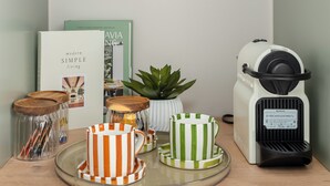 Una cocina con cafetera, tazas en un escurreplatos y una bandeja con vasos y una planta.