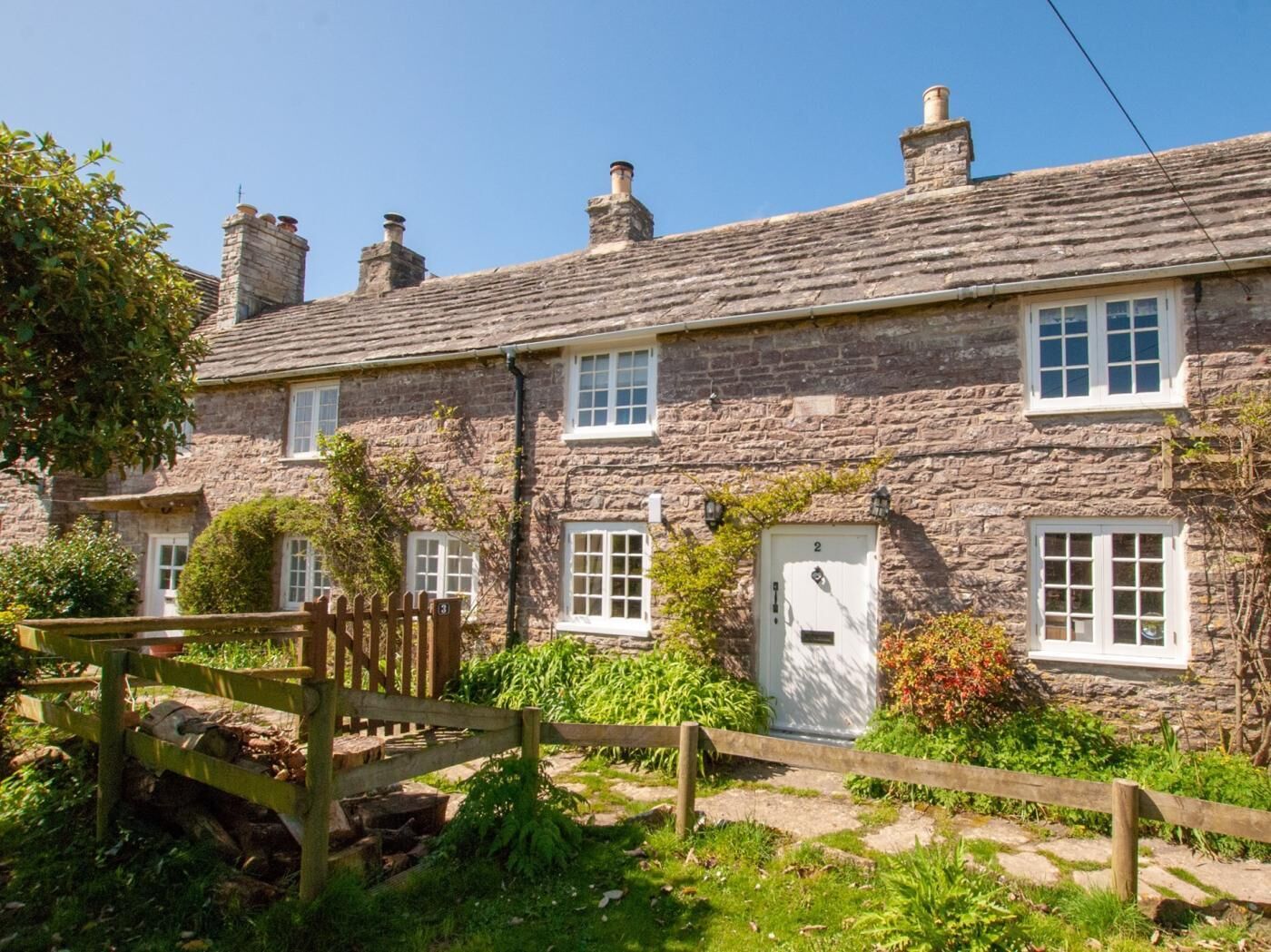 A stone cottage with multiple windows, a wooden gate, and a small garden.