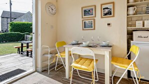 Un'area pranzo con un tavolo apparecchiato per quattro persone, sedie, una sveglia e quadri appesi al muro.