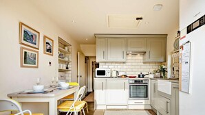 Una cucina con mobili bianchi, un tavolo da pranzo con sedie, un forno a microonde, un forno e un frigorifero.
