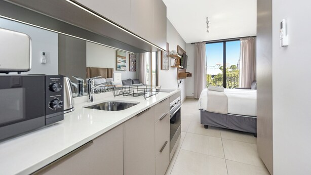 Une cuisine moderne équipée d’un four à micro-ondes, d’une cuisinière et d’un évier. La chambre comprend un lit avec vue sur la ville.