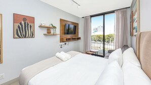 Une chambre d’hôtel moderne dotée d’un grand lit, d’une télévision à écran plat, d’un balcon offrant une vue sur la ville et d’œuvres d’art accrochées aux murs.