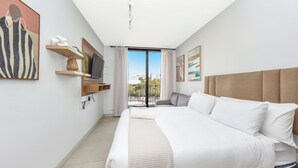 Une chambre d’hôtel moderne avec un grand lit, un téléviseur fixé au mur, un balcon avec vue et un tableau au mur.