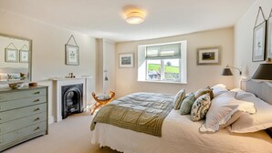 A bedroom with a fireplace, a bed with multiple pillows, a dresser, and a window with a view. - 1 Bed in Ashprington (oc-h41748) (Ashprington)