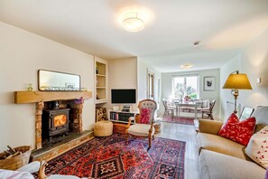 A cozy living room with a fireplace, a TV, a dining area, and a sofa. - 1 Bed in Ashprington (oc-h41748) (Ashprington)