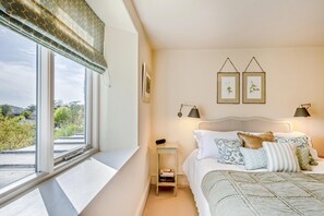 A bedroom with a large window, a bed with multiple pillows, two wall-mounted lamps, and framed pictures. - 1 Bed in Ashprington (oc-h41748) (Ashprington)
