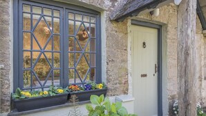 A stone building with a window featuring a diamond pattern, a white door, and a small porch area with plants. - 1 Bed in Ashprington (oc-h41748) (Ashprington)
