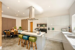 A modern kitchen with white cabinets, a central island with stools, and a dining area with a wooden partition. - 4 Bed in Acton (oc-k40259) (Acton Town)