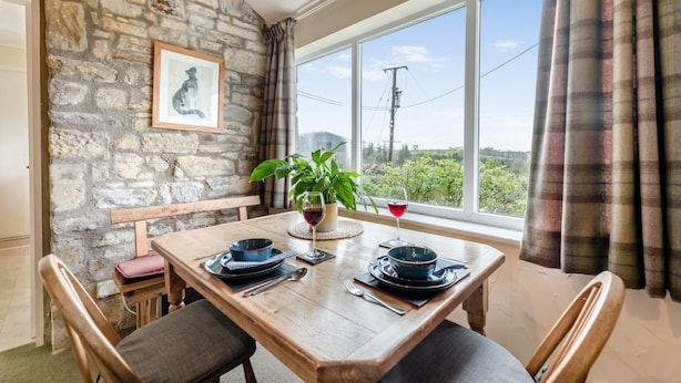 A dining area with a stone wall, a framed picture, a table set with plates, a glass of red wine, and a potted plant. - 1 Bed in Edlingham (oc-g41396) (Edlingham)