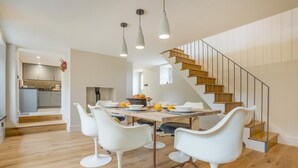 Eine moderne Küche mit weißen Schränken, ein Essbereich mit einem Holztisch und weißen Stühlen sowie eine Treppe mit Holzstufen und Metallgeländern.