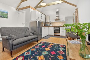 A cozy living area with a sofa, a patterned rug, and a dining table with a vase of flowers. - 1 Bed in Manaccan (oc-b42477) (Porthallow)