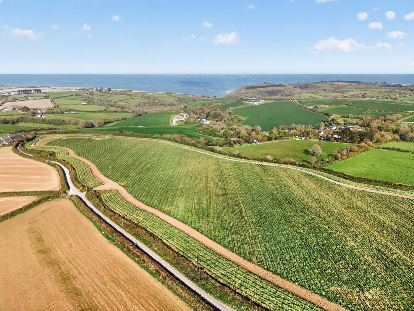 An aerial view of a rural landscape with fields, a road, and a distant coastline.