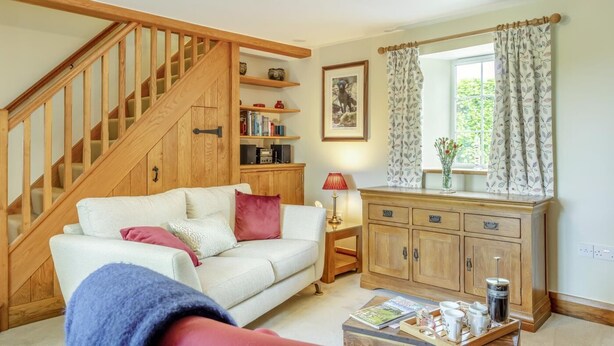 Un salon chaleureux avec un escalier en bois, un canapé, un meuble en bois et une fenêtre avec des rideaux.