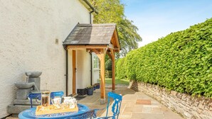 Une terrasse avec une table préparée pour le thé, une petite construction en bois et un mur de pierre.