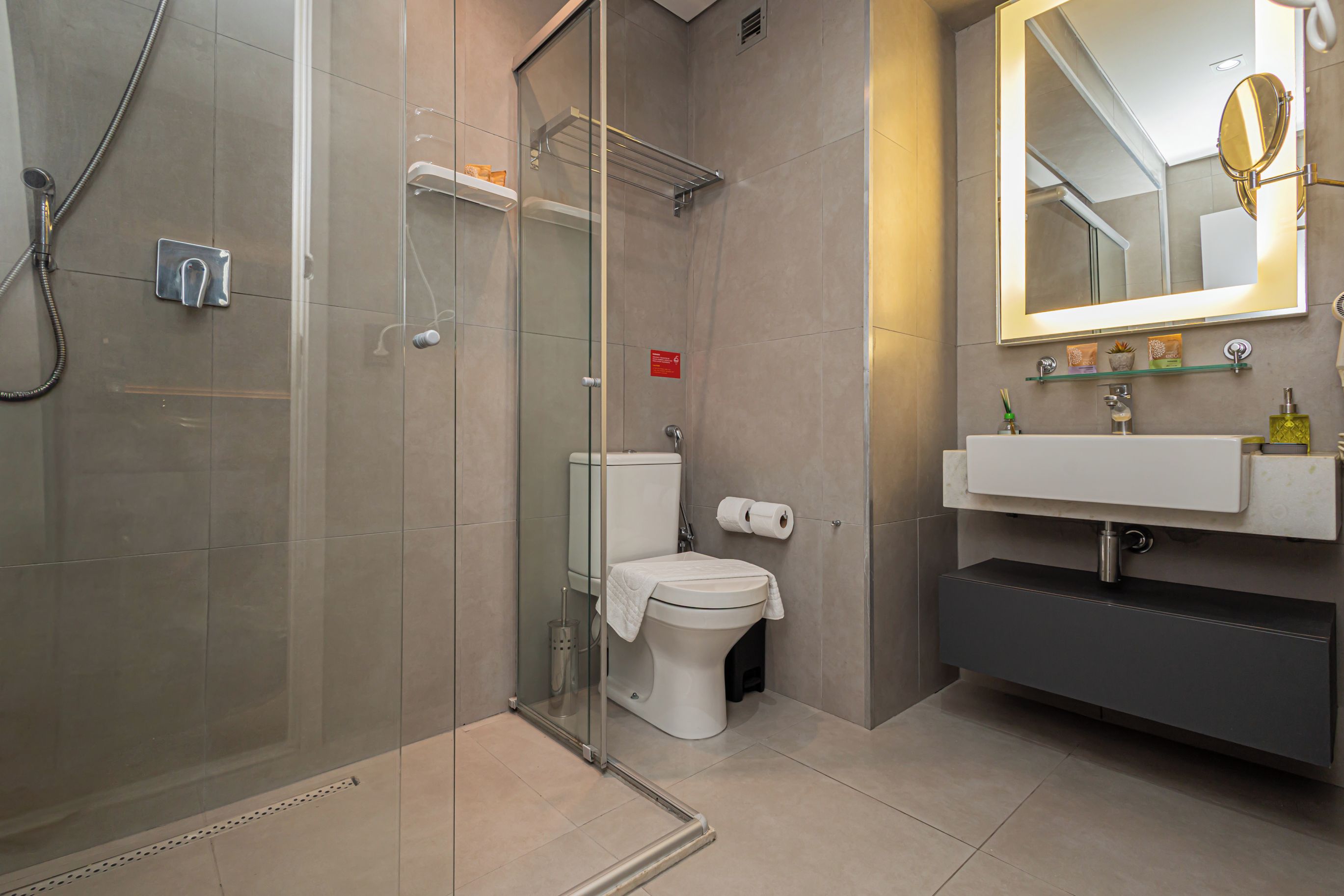 A modern bathroom with a glass shower enclosure, a toilet, a sink with a mirror, and a towel rack.