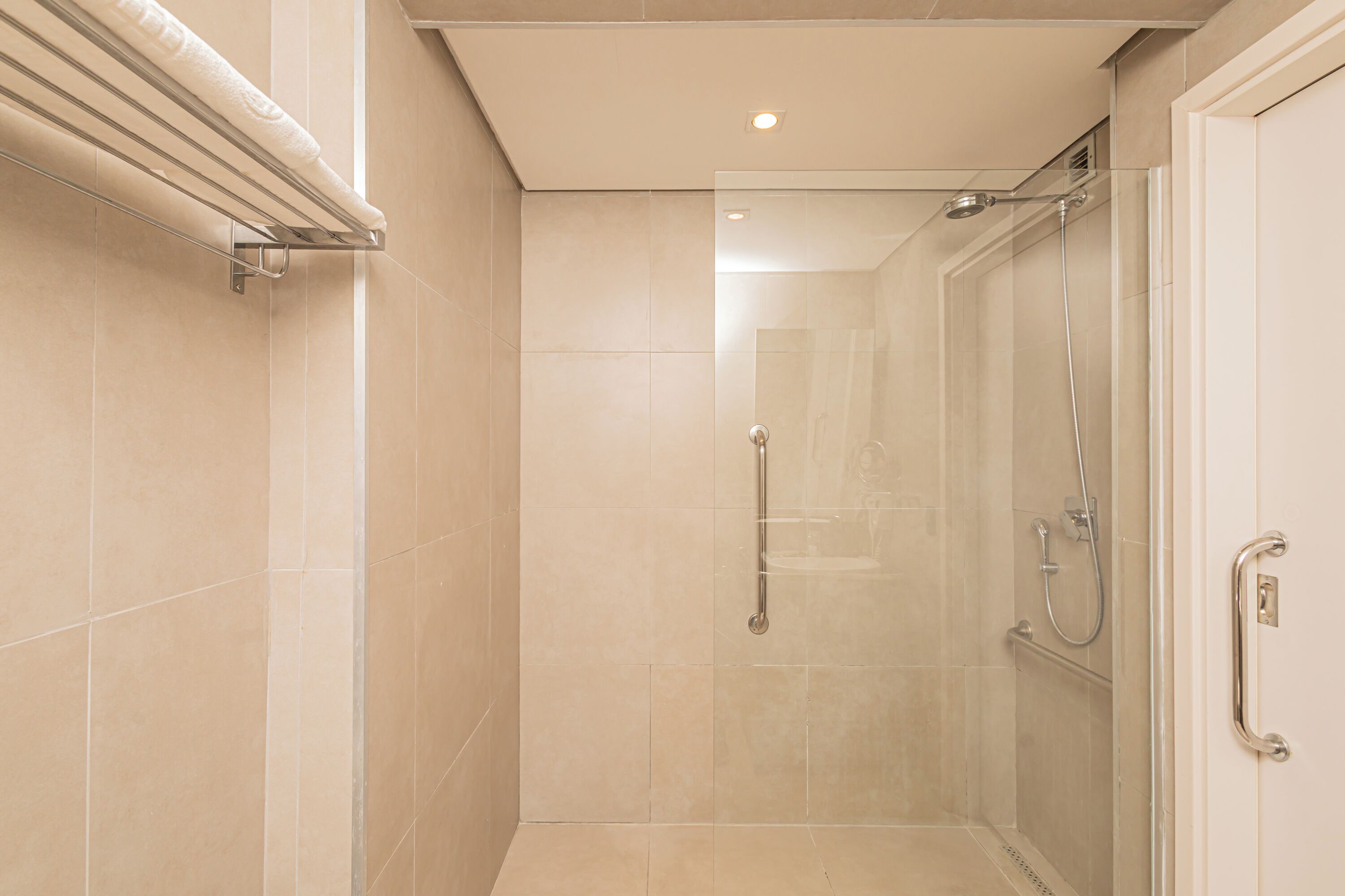 Une douche avec une porte en verre, une barre d’appui et un porte-serviettes.
