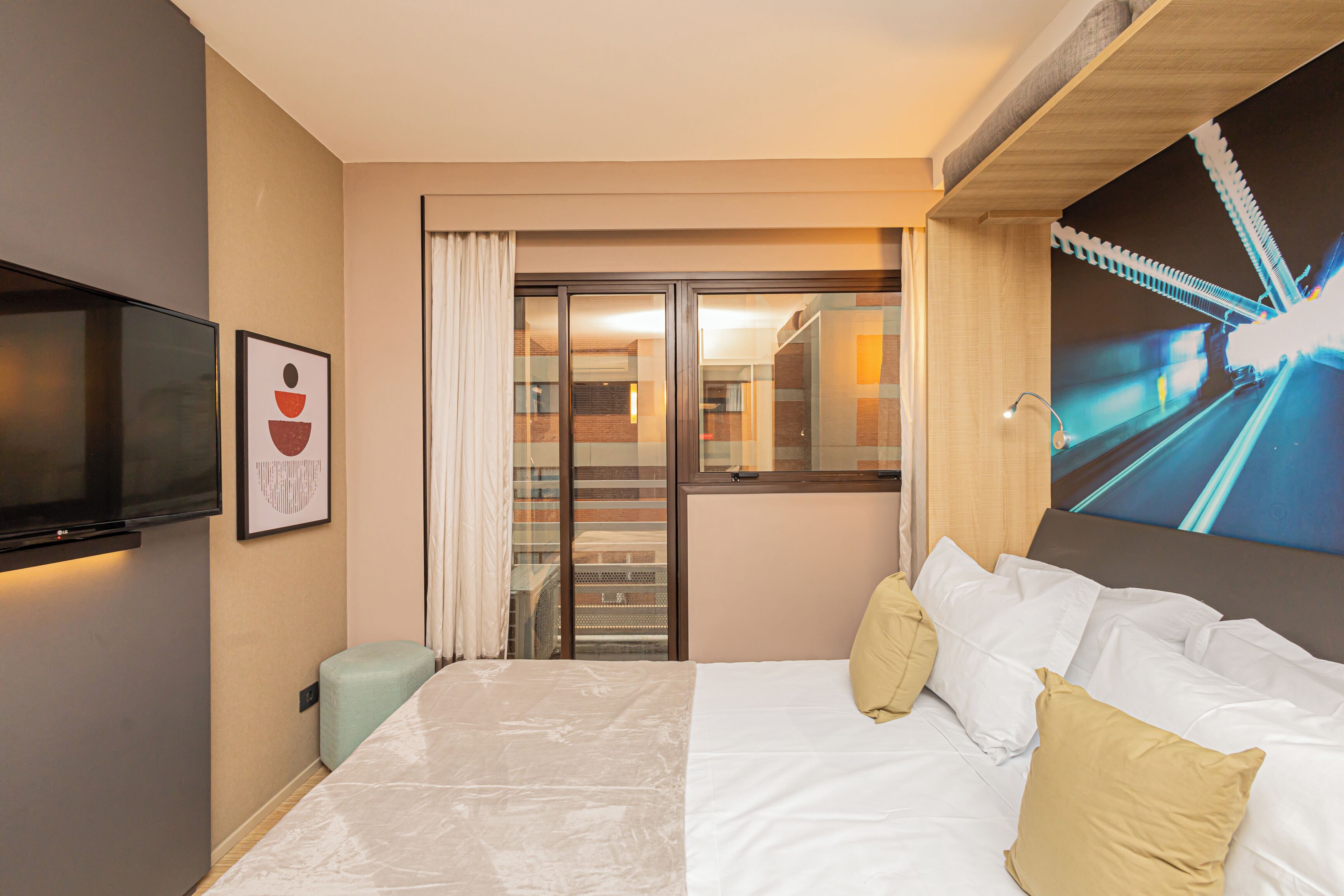 Une chambre d’hôtel avec un lit, un téléviseur à écran plat, un tableau et une grande fenêtre donnant sur un pont.