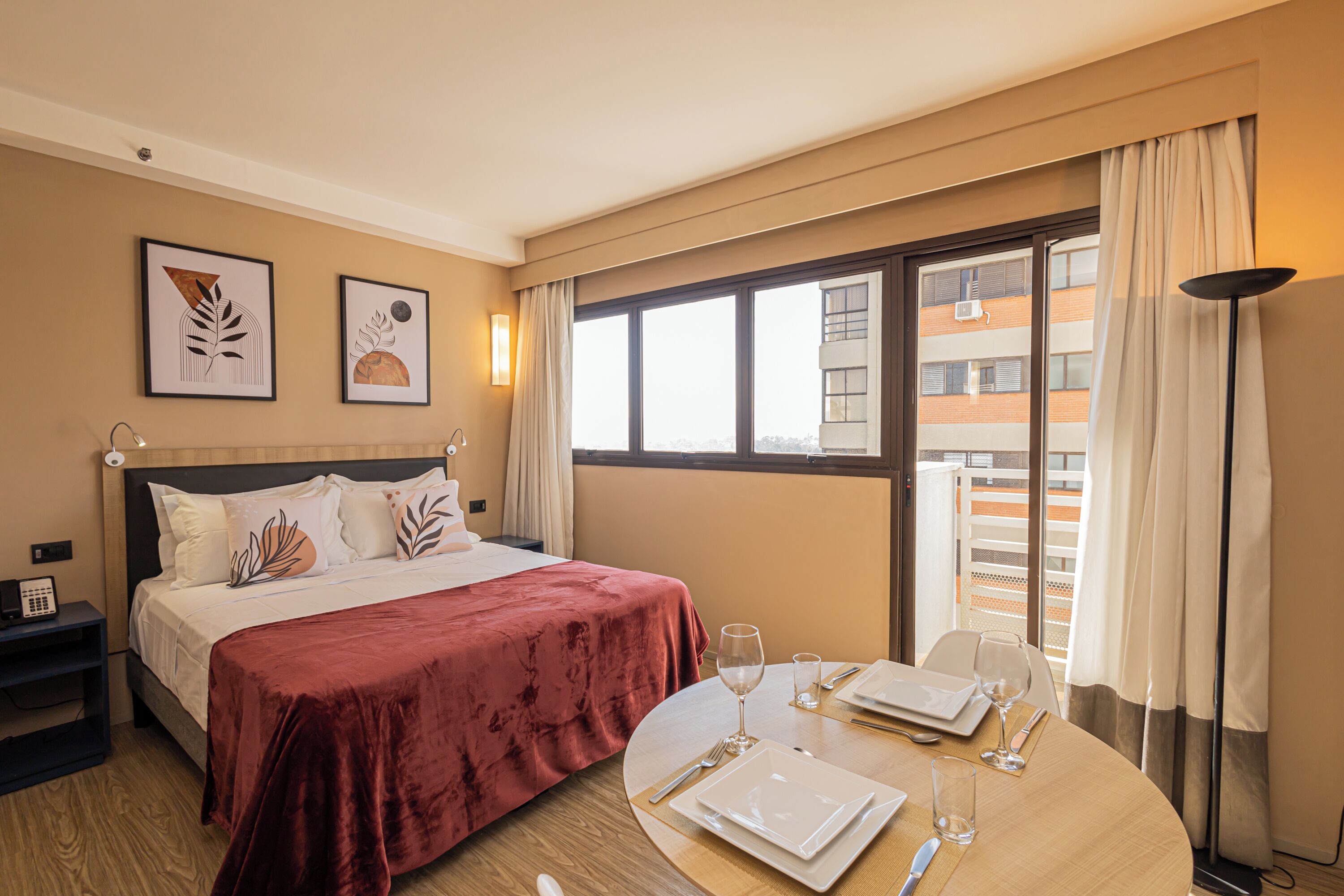 Een hotelkamer met een bed, een eettafel gedekt voor twee personen en een raam met uitzicht op gebouwen.