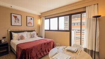 Een hotelkamer met een bed, een eettafel gedekt voor twee personen en een raam met uitzicht op gebouwen.