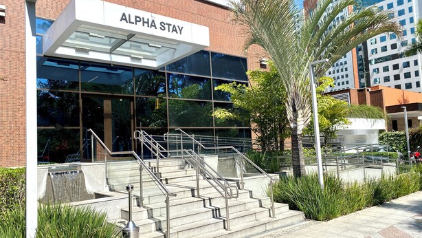 A building with a sign reading 'ALPHA STAY' and a set of stairs leading to the entrance.